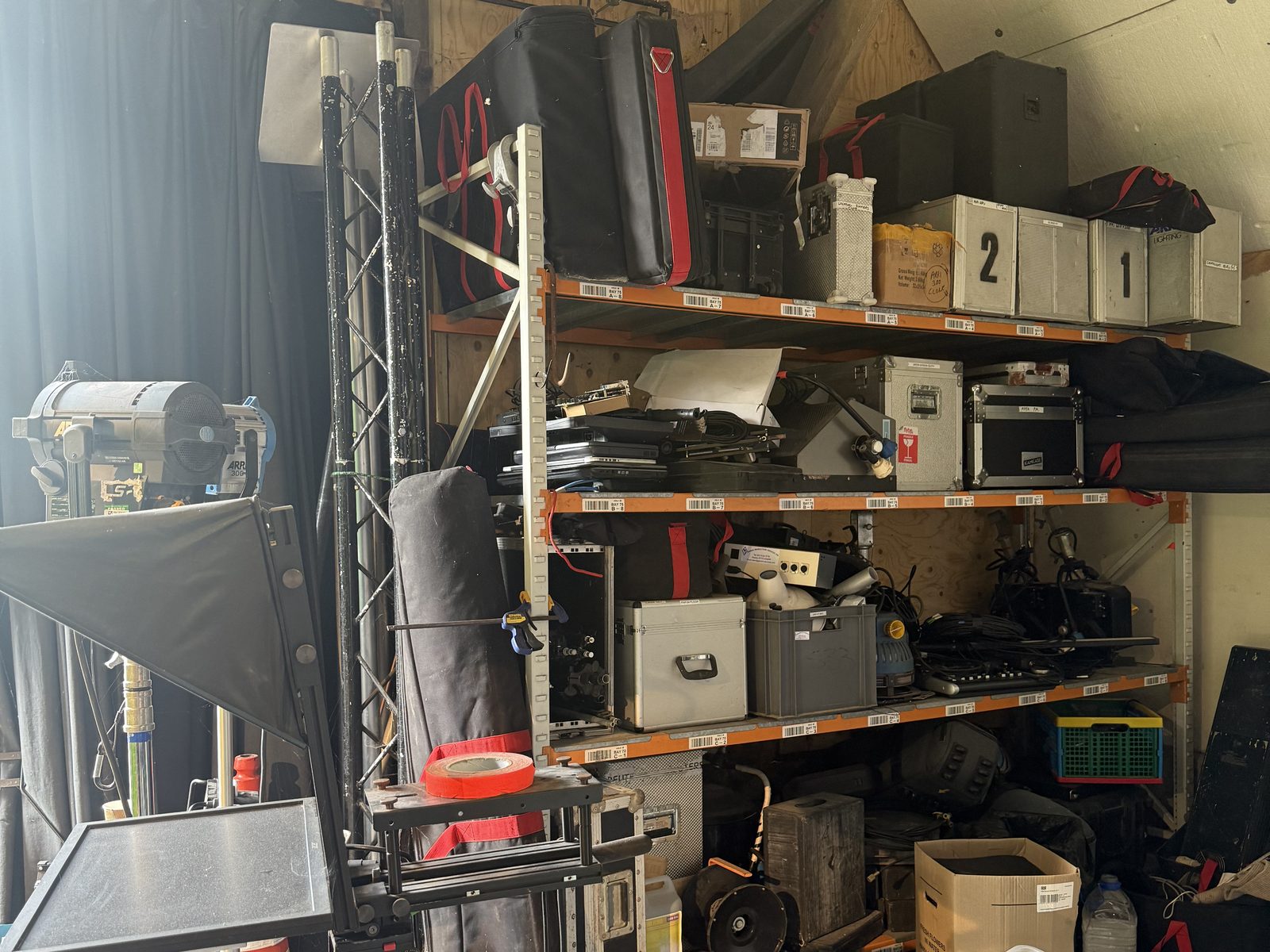 The kit store at the studio: flight cases, lamps and a prompter on racking